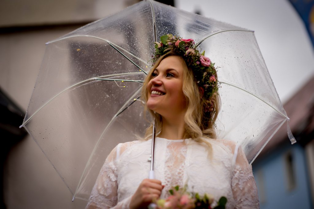 Braut lächelt unter einem transparenten Regenschirm am Hochzeitstag