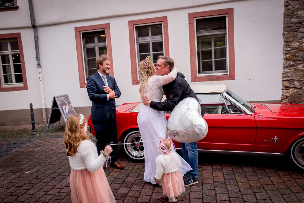 Brautpaar posiert mit dem roten Hochzeitsauto vor dem Standesamt Oberursel