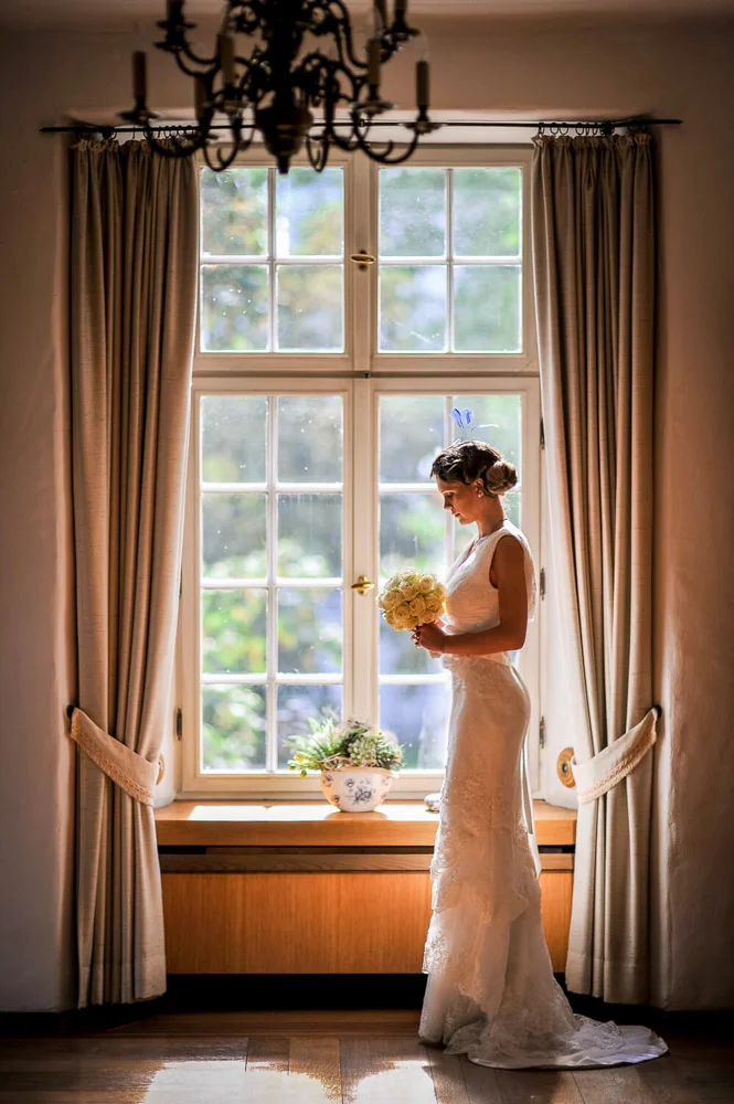 Braut schaut aus dem Fenster – künstlerische Hochzeitsfotografie Frankfurt.